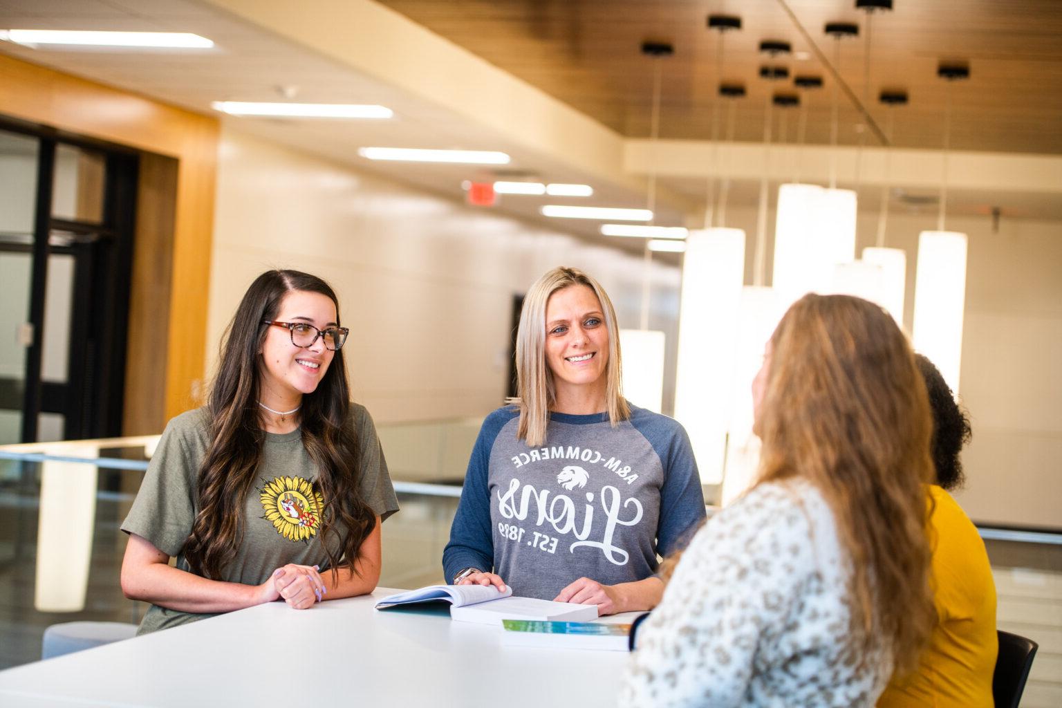 A group of 4 females talking with a book open on a table.