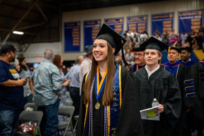 A female student smiling while walking down the aisle during graduating