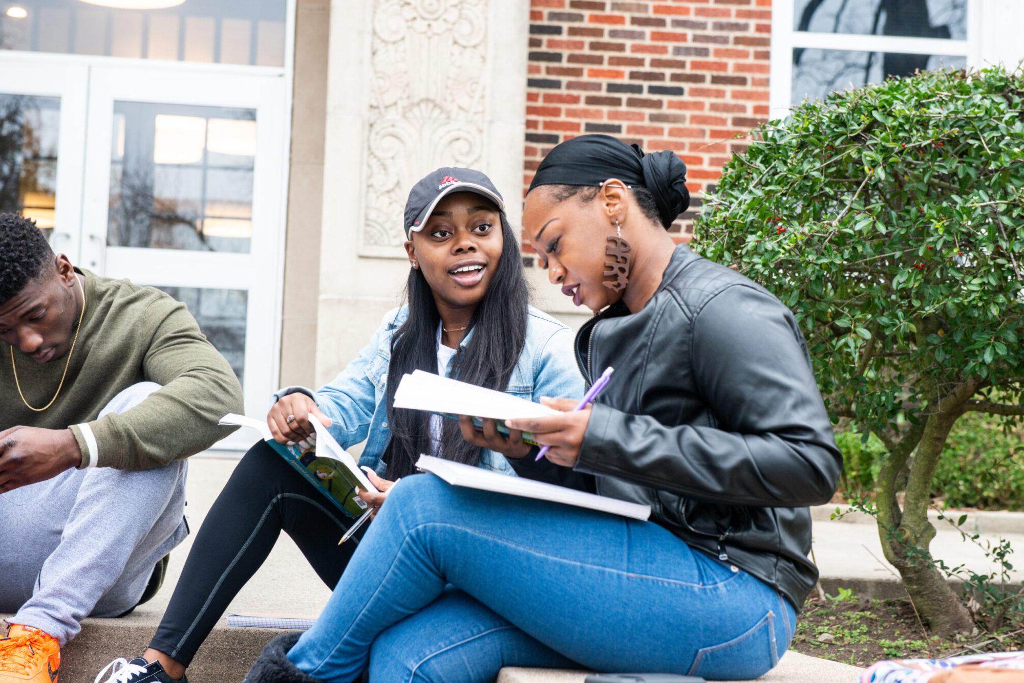 Two female student outside a building completing a school assignment.