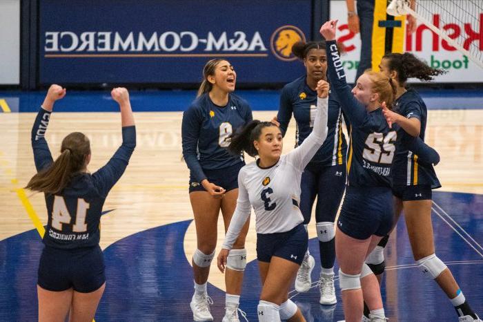 Six volleyball players cheer as they break from a huddle, with arms raised.