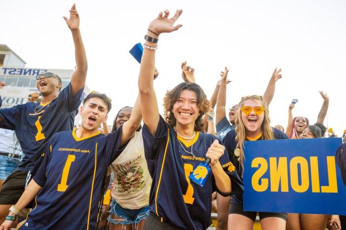 学生 cheer on the football team from the stands with arms raised.