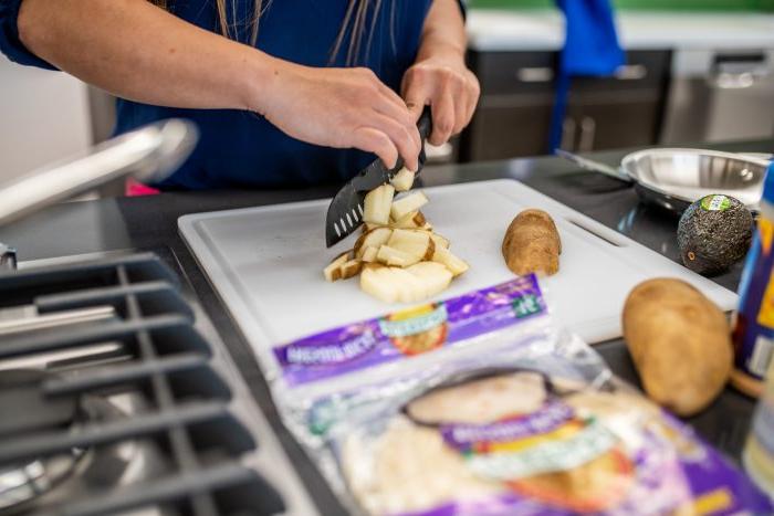 Hands pictured using a knife to cut potatoes.